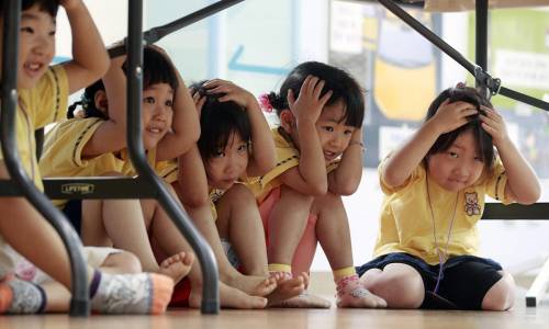 Delle bambine si riparano sotto i banchi durante un'esercitazione per apprendere come comportarsi in caso di terremoto, in una scuola materna di Seul in Corea del Sud. 